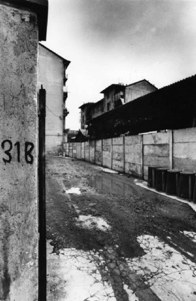 Milano. Scorcio dell'interno di un cortile con muro di cinta in cemento e sullo sfondo edifici residenziali e industriali