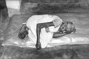 India. Anziano denutrito dorme a terra su di un materasso ricoperto di plastica