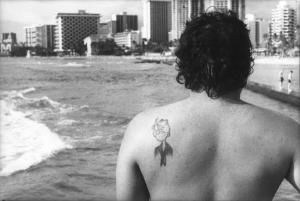 Hawaii. Uomo di spalle con il tatuaggio di Popeye/Braccio di Ferro sulla scapola - sullo sfondo i palazzi sulla spiaggia