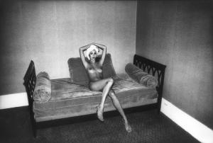 Parigi. Modella nuda con asciugamano avvolto in testa e sandali seduta sul letto di una camera d'albergo