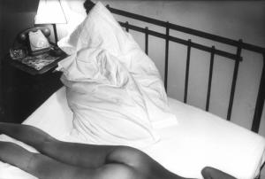 Particolare di un corpo femminile sdraiato su di un letto in una camera d'albergo - sullo sfondo il comodino con telefono, posacenere e abat-jour