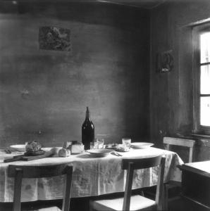 Interno di abitazione - Sala da pranzo - tavolo imbandito con bottiglia di vono, insaccato, pane, piatti e posate