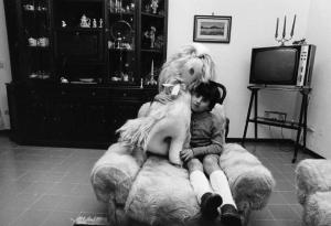 Terni - Quartiere Matteotti. Bambino in posa sulla poltrona del soggiorno, abbracciato a un grosso animale di pelouche