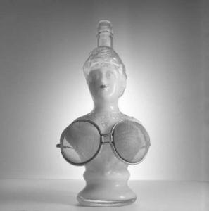 Bottiglia scultorea a forma di busto, con occhiali formati da colini