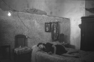 Italia Dopoguerra: Valmontone bombardata. Valmontone - Abitazione, interno - Ritratto femminile: donna distesa sul letto - Comodini in legno - Immagini religiose alla parete