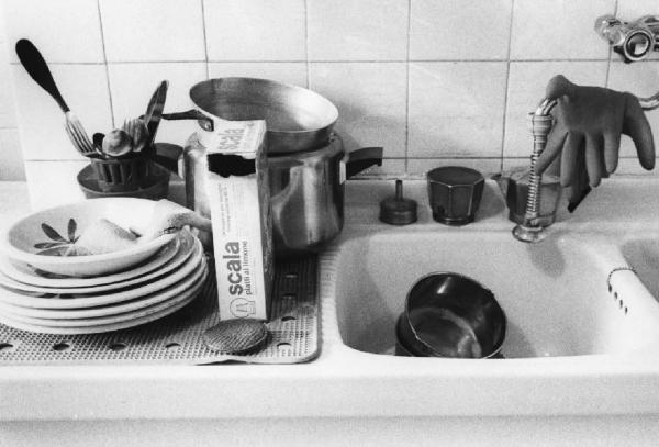Una, nessuna, centomila. Gli oggetti della pulizia. Milano - Cucina, interno - Lavello con stoviglie, pentole e caffettiera - Detersivo, guanti - Pulizie