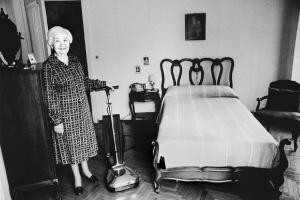 Una, nessuna, centomila. La Casa e i Riti. Milano - Camera da letto, interno - Ritratto femminile: donna anziana con aspirapolvere
