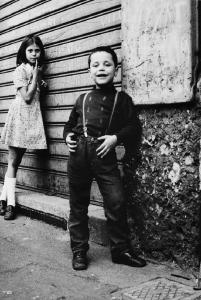 Bambini in Piazzale Dateo. Milano, Piazzale Dateo - Ritratto di coppia: bambino in posa e bambina appoggiata ad una saracinesca abbassata