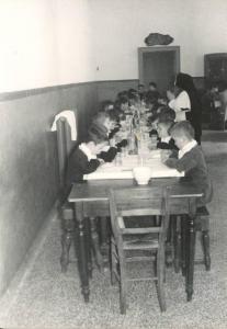 Istituto dei Ciechi di Milano - Refettorio maschile - Bambini seduti intorno a un tavolo apparecchiato - Suora