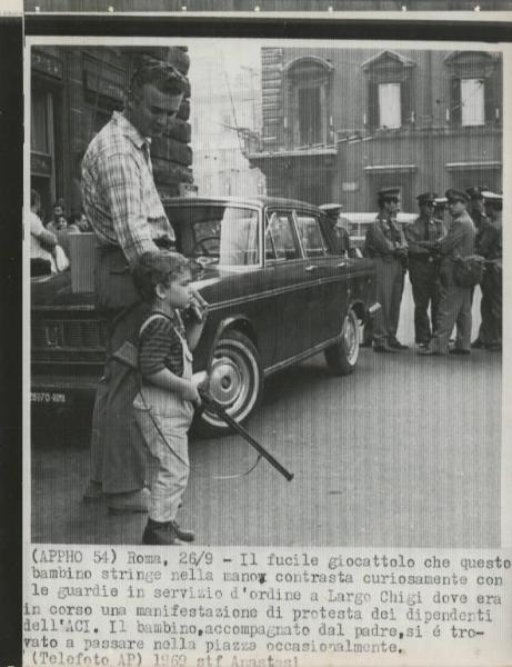 Roma - Largo Chigi - Bambino con fucile giocattolo accompagnato dal padre - Forze dell'ordine - Automobile