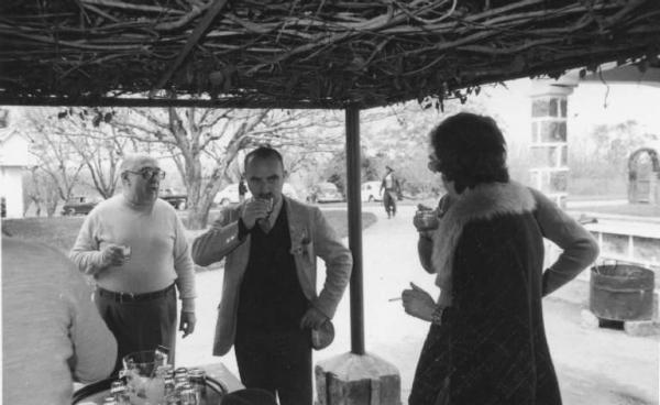 Il regista Alberto Lattuada beve da un bicchiere tra persone non identificate