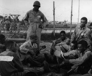 Set del film "Senza pietà" - Regia Alberto Lattuada - 1948 - Il regista Alberto Lattuada suona la chitarra seduto tra un gruppo di soldati in divisa militare