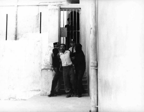 Scena del film "La battaglia di Algeri" - Regia Gillo Pontecorvo - 1966 - Due agenti di polizia osservano due uomini da volto coperto trascinare il condannato