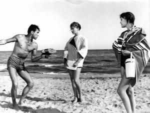 Scena del film "Amore a prima vista" - Regia Franco Rossi - 1957 - L'attore Walter Chiari in costume da bagno con le scarpe in mano e due attrici non identificate sulla spiaggia