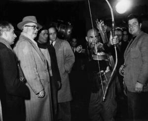 Set del film "Attila" - Regia Pietro Francisci - 1954 - Il regista Pietro Francisci con la troupe e un attore non identificato in costume armato di arco e frecce