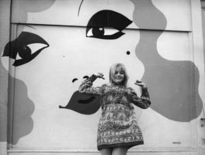 Scena del film "Col cuore in gola" - Regia Tinto Brass - 1967 - L'attrice Ewa Aulin in piedi davanti a un murales