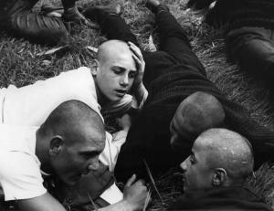 Scena del film "La commare secca" - Regia Bernardo Bertolucci - 1962 - Gruppo di giovani attori non identificati con testa rasata sdraiati su un prato.