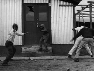 Scena del film "Congo vivo" - Regia Giuseppe Bennati - 1961- Attori non identificati cercano di lapidare un soldato all'esterno di un capanno