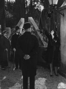 Set del film "Corte d'assise" - Regia Guido Brignone- 1930- Un gruppo di attori non identificati osserva l'attrice Marcella Albani che tocca una giacca appesa ad un lampione.