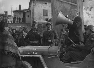 Fotografia del film "Cuori senza frontiere" - Regia Luigi Zampa 1950 - Un attore non identificato detta un annuncio da un'auto militare, intorno gruppi di attori non identificati.