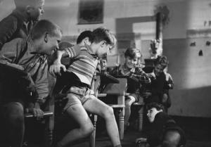 Fotografia del film "Cuori senza frontiere" - Regia Luigi Zampa 1950 - Un gruppo di bambini sui banchi di scuola si volta verso l'attore Enzo Staiola caduto a terra.