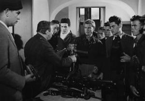 Fotografia del film "Cuori senza frontiere" - Regia Luigi Zampa 1950 - L'attore Erno Crisa con un gruppo di attori non identificati attorno ad un tavolo pieno di armi.