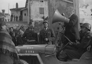 Fotografia del film "Cuori senza frontiere" - Regia Luigi Zampa 1950 - Un attore non identificato detta un annuncio da un'auto militare, intorno gruppi di attori non identificati.