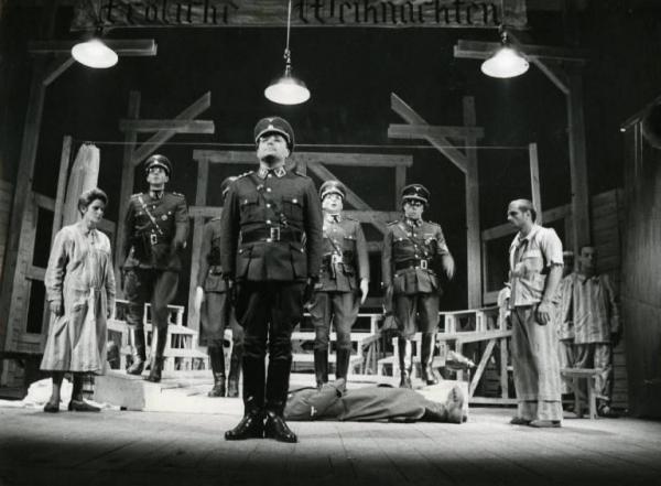 Sul palco dello spettacolo teatrale "Il dio Kurt" - Regia Antonio Calenda, stagione 1968/69 - Alida Valli a sinistra e Luigi Diberti a destra, guardano il corpo di un uomo che giace sul pavimento al centro del palco. Intorno a loro, soldati nazisti.