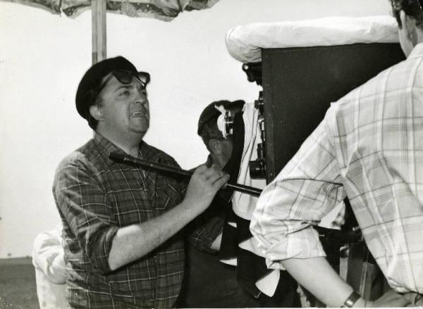 Sul set del film "La dolce vita" - Regia Federico Fellini, 1960 - Mezza figura: Federico Fellini, in piedi, dietro alla macchina da presa.