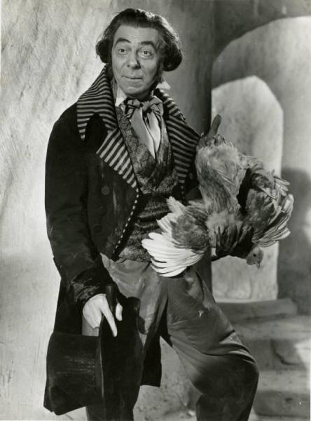 Scena del film "Don Buonaparte" - Regia Flavio Calzavara, 1941 - Piano americano frontale di Aldo Silvani. L'attore ha nella mano destra una bottiglia di vino e un cilindro e, nella mano sinistra una gallina.