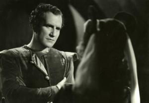 Scena del film "Dente per dente" - Regia Marco Elter, 1943 - Mezza figura di Carlo Tamberlani, con le braccia incrociate sul petto, mentre ascolta una donna di spalle di fronte a lui.
