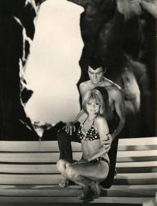 Scena del film "Diabolik" - Regia Mario Bava, 1968 - Marisa Mell accovacciata in bikini. Alle sue spalle, John Phillip Law, chinato, ha una mano appoggiata al braccio di lei e la guarda.