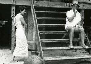 Sul set del film "La diga sul Pacifico" - Regia René Clément, 1957 - Silvana Mangano, di profilo, scalza e avvolta in un asciugamano. Accanto, su una scalinata in legno, è seduto il regista René Clement, con l'indice destro davanti alla bocca.