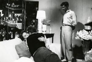 Sul set del film "La diga sul Pacifico" - Regia René Clément, 1957 - Il regista René Clément, di spalle, abbraccia Alida Valli seduta su un divano. Sulla destra, Anthony Perkins, in piedi, osserva la scena.