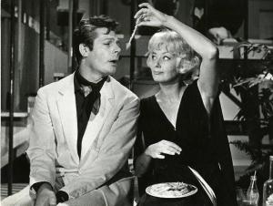 Scena del film "La dolce vita" - Regia Federico Fellini, 1960 - Marcello Mastroianni, seduto, con le mani in grembo, apre la bocca. Christine Denise, seduta al suo fianco, alza un braccio sopra la testa e gli porge del pollo.
