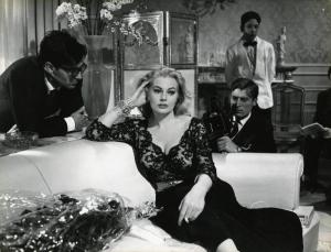 Scena del film "La dolce vita" - Regia Federico Fellini, 1960 - Anita Ekberg, seduta su un divano, fuma e appoggia un braccio allo schienale tenendosi la testa. Dietro di lei, Giulio Paradisi. A sinistra, Sandy von Norman.