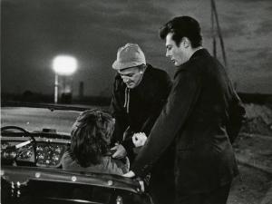 Sul set del film "La dolce vita" - Regia Federico Fellini, 1960 - Federico Fellini mostra a Marcello Mastroianni come prendere per il bavero Yvonne Furneaux seduta, di spalle, in una decappottabile.