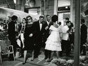 Scena del film "La dolce vita" - Regia Federico Fellini, 1960 - Al centro, Anouk Aimée, con occhiali da sole, cammina. Alle sue spalle, Marcello Mastroianni. Intorno a loro, attori non indentificati.