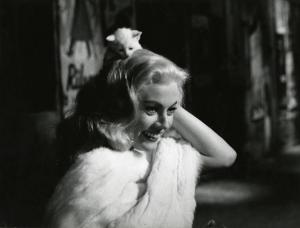 Scena del film "La dolce vita" - Regia Federico Fellini, 1960 - Mezza figura, di tre quarti, di Anita Ekberg con un gattino sulla testa. L'attrice lo tiene con una mano e sorride.