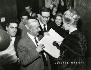 Sul set del film "La dolce vita" - Regia Federico Fellini, 1960 - Mezza figura, di profilo, di Anita Ekberg alla presentazione del film in anteprima alla stampa presso la Terrazza Martini. L'attrice sta firmando un libro.