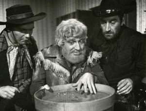 Scena del film "Un dollaro di fifa" - Regia Giorgio Simonelli, 1960 - Mezza figura di Ugo Tognazzi nei panni di un cercatore d'oro. L'attore è al centro, tra due attori non identificati vestiti da cowboys.