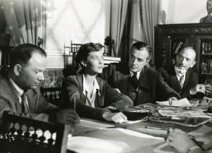 Scena del film "Domani è troppo tardi" - Regia Léonide Moguy, 1950 - Mezza figura di Lois Maxwell e Vittorio De Sica seduti a una scrivania tra altri due uomini.