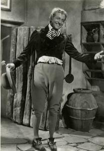 Scena del film "Don Buonaparte" - Regia Flavio Calzavara, 1941 - Figura intera frontale di Osvaldo Valenti. L'attore sorride e allarga le braccia, nella mano destra tiene un cappello e un fiore.