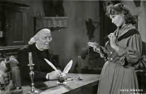 Scena del film "Don Buonaparte" - Regia Flavio Calzavara, 1941 - Ermete Zacconi, seduto a una scrivania guarda Oretta Fiume, in piedi davanti lui. L'attrice ha in mano un ago e un punta spilli.