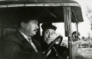 Scena del film "Don Camillo" - Regia Julien Duvivier, 1952 - Primo piano di profilo di Gino Cervi alla guida di un pulmino e di Fernandel, frontale, seduto al suo fianco.