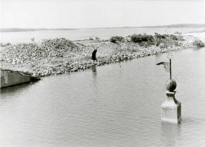 Scena del film "Don Camillo" - Regia Julien Duvivier, 1952 - Campo lungo. Una donna in piedi sulla riva di un fiume. Dal corso d'acqua spunta la cima di un campanile.