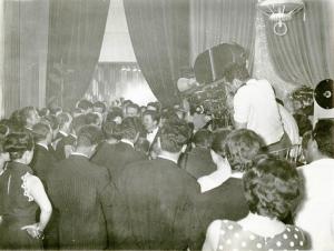 Sul set del film "La donna del giorno" - Regia Francesco Maselli, 1957 - Totale di un folto gruppo di uomini e donne assiepato davanti all'uscita di una platea teatrale. Sulla destra, un operatore, li riprende dall'alto.