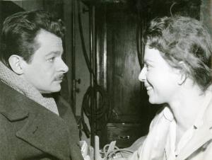 Sul set del film "La donna del giorno" - Regia Francesco Maselli, 1957 - Primo piano, di profilo di Serge Reggiani, mentre guarda una donna di fronte a lui che gli sorride.