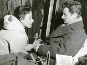 Sul set del film "La donna del giorno" - Regia Francesco Maselli, 1957 - Mezza figura, di profilo di Serge Reggiani, seduto, con gli occhi chiusi. Di fronte a lui, è seduta una donna con una sigaretta in mano.
