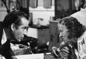 Scena del film "La donna scimmia" - Regia Marco Ferreri, 1964 - Ai lati opposti di un tavolo, primo piano di profilo di Ugo Tognazzi ed Ermelinda De Felice che si sporgono in avanti e si guardano negli occhi.